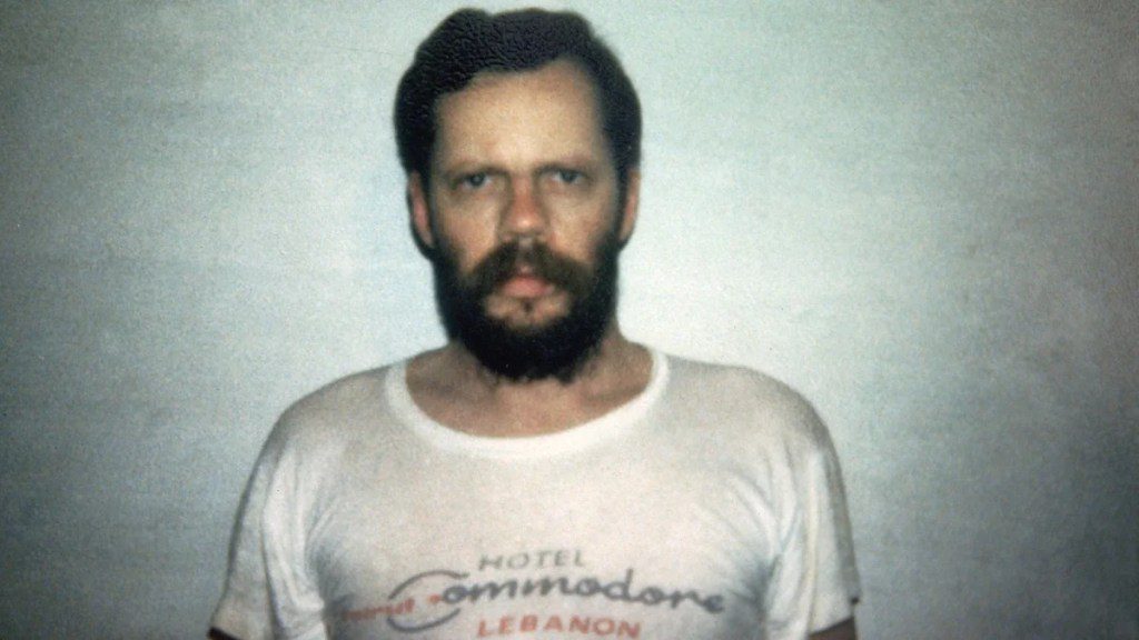 A man with a beard stands posing for a photo. He has light-toned skin. His T-shirt reads "Hotel Commodore, Lebanon."